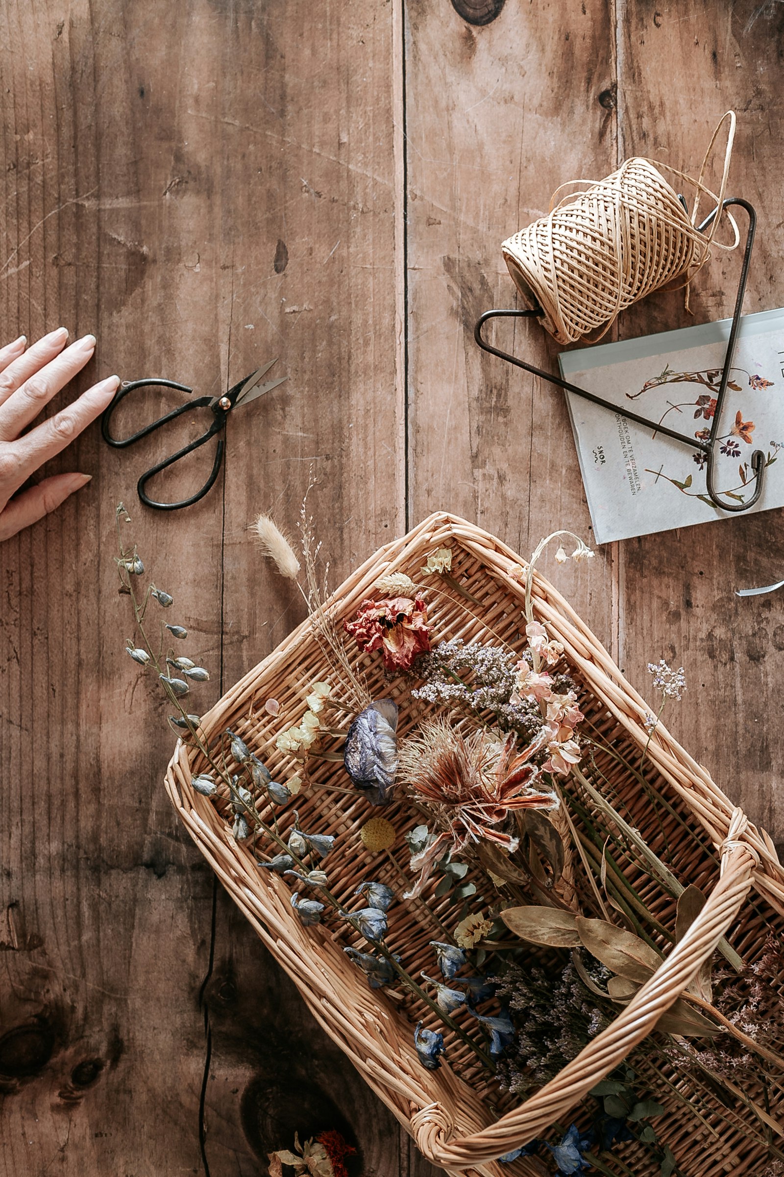 A workbench with a basket of dried flowers, scissors and twine